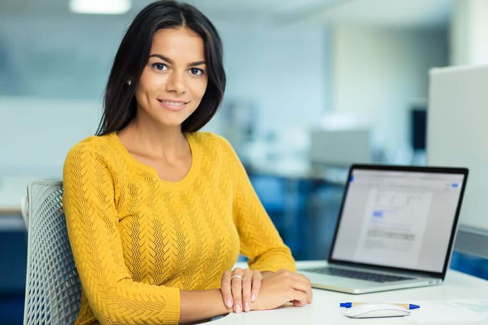Portrait of a happy casual businesswoman in sweater sitting at her workplace in office-1-2