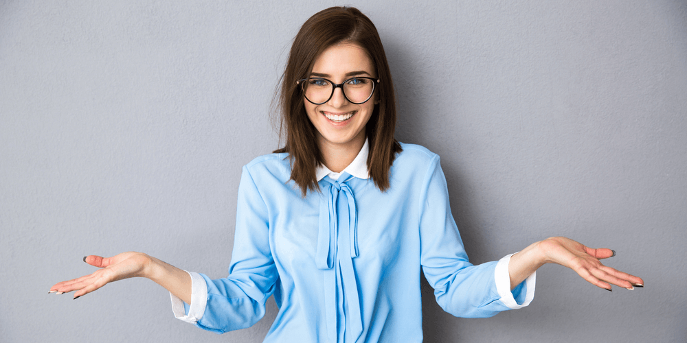 Smiling businesswoman in gesture of asking over gray background. Looking at camera. Wearing in blue shirt and glasses 1000x500